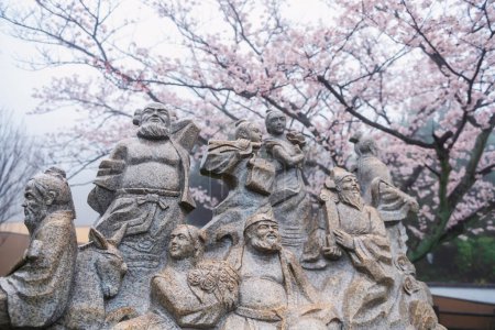 Statue von acht Unsterblichen, eine Gruppe legendärer Xian Unsterblicher in der chinesischen Mythologie gegen rosa Sakura-Blüte des Kirschbaums im Beppu Memorial Park, Oita, Kyushu, Japan.