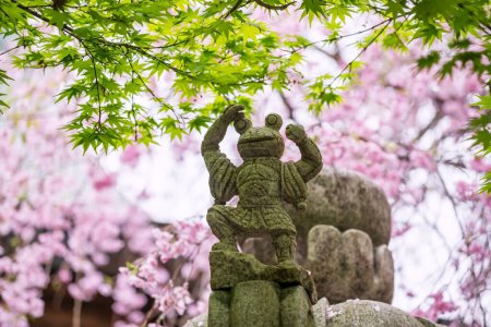 Frog statue on roof with green maple and pink sakura blossom cherry tree at Nyoirinji Temple, Ogori, Fukuoka, Japan. Here is famed for toad statue referred to as Kaeru dera, while the formal name is Seieizan Nyoirin-ji.