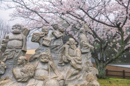 ocho Inmortales estatua, un grupo de legendario Xian inmortal en la mitología china contra flor de cerezo rosa de árbol de sakura y niebla en el parque conmemorativo de Beppu, Oita, Kyushu, Japón.