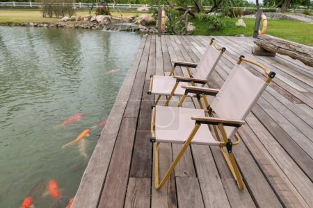 Chairs on wood pergola by carp fish pond in spring garden of tropical resort.