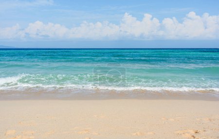 Téléchargez les photos : Plage de sable avec vague calme ondulante de l'océan par une journée ensoleillée sur fond de nuages blancs dans le ciel bleu - en image libre de droit