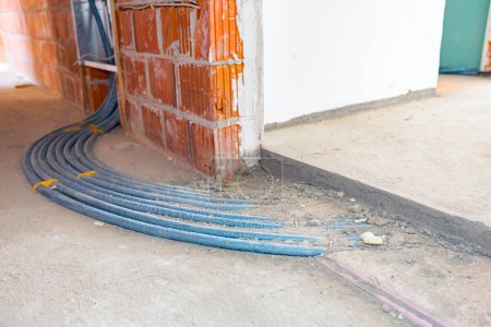 New distribution system mounted for central heating floor in a residential building under construction. Pile of blue pipelines passing through the concrete floor.