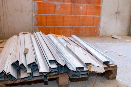 Foto de Montón de nuevos perfiles metálicos para paneles de yeso dispuestos en paleta de madera, galvanizados y esperando ser instalados. - Imagen libre de derechos