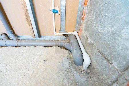 Foto de Nueva instalación de agua, tuberías de alcantarillado de PVC gris montadas a la vista montadas en la pared de yeso. - Imagen libre de derechos