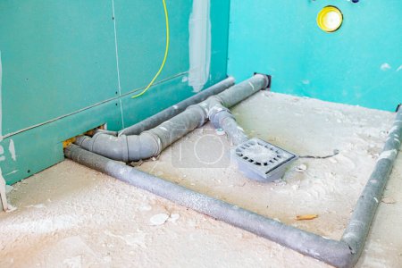 Foto de Instalación de agua en el nuevo baño sin terminar, tuberías de alcantarillado de PVC gris montadas a la vista montadas en el lugar para una cabina de ducha. - Imagen libre de derechos