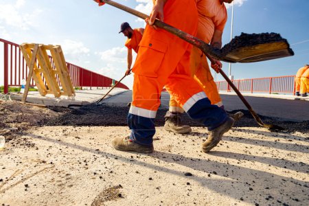 Photo for Few workers are using shovels to level, set up layer of fresh tarmac to right measures, pouring hot asphalt. - Royalty Free Image