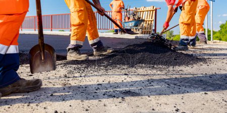 Pocos trabajadores están utilizando palas para nivelar, configurar la capa de asfalto fresco a las medidas correctas, verter asfalto caliente.
