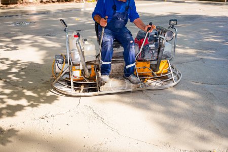 Photo for Worker sitting on a self-leveling power trowel machine with gas engine has wheels with pads, plate and he is driving it in circles smoothing surface on concrete slab. - Royalty Free Image