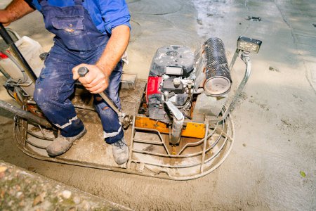Photo for Worker sitting on a self-leveling power trowel machine with gas engine has wheels with pads, plate and he is driving it in circles smoothing surface on concrete slab. - Royalty Free Image