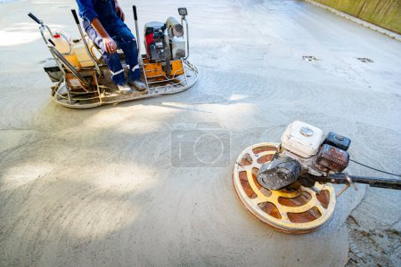 Photo for Two types of self-leveling power trowel machine with gas engine have wheels with pads, plate and he is driving it in circles smoothing surface on concrete slab. - Royalty Free Image
