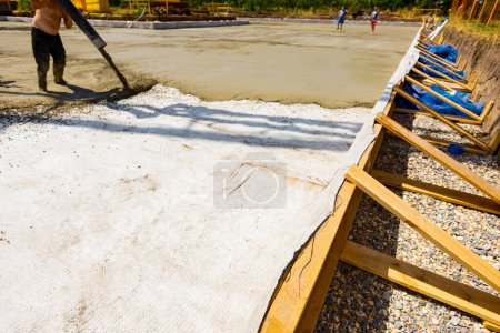 Photo for The edge of foundation mold built with painted yellow wooden planks. Worker directs pump on right direction, pours layer of concrete in build base covering square reinforcement. - Royalty Free Image