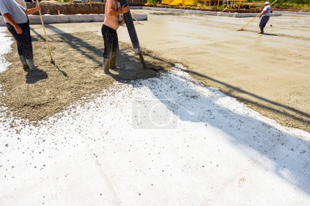 Photo for Construction worker is directing the pump tube on right direction, pouring layer of concrete in building foundation covering square reinforcement, another workman checks the height of the concrete with wooden tool. - Royalty Free Image