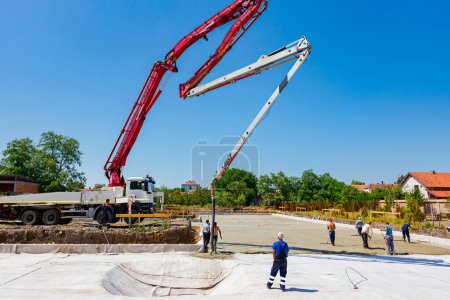 Photo for Construction site, mixer truck pouring concrete into pump machine pumping to exit tube, worker directs it on the right direction, building foundation. Riggers, workers leveling concrete - Royalty Free Image