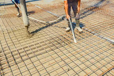 Photo for Worker is using vibration power tool, compactor, for compacting fresh liquid concrete, flowing slowly among square reinforcement in the base of new building - Royalty Free Image