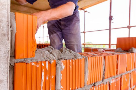 Photo for Mason, bricklayer worker is using red blocks to mount a wall at construction site. - Royalty Free Image
