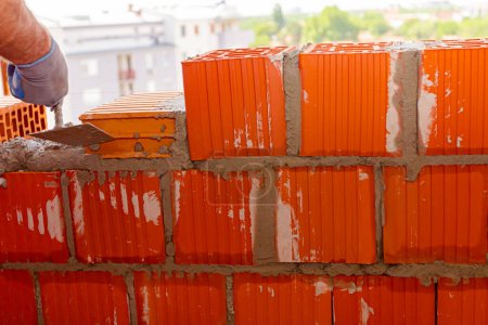 Foto de El trabajador está utilizando espátula, llana, para aplicar mortero en bloques rojos para hacer la pared, albañil. El edificio está en construcción. - Imagen libre de derechos