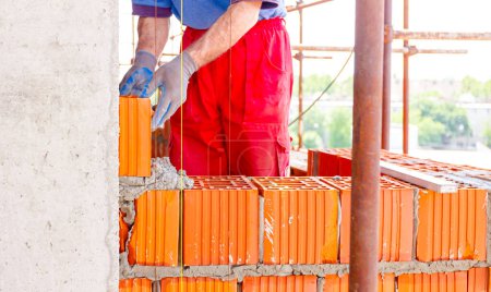 Foto de Mason, albañil trabajador está utilizando bloques rojos para montar una pared al lado de la línea de cuerda para ser recta. - Imagen libre de derechos
