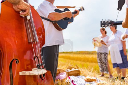 Téléchargez les photos : La contrebande est au centre. Contrebassiste musicien joue de la contrebasse pour le bonheur et le succès avant que les agriculteurs commencent à récolter les céréales manuellement de manière rurale traditionnelle. - en image libre de droit
