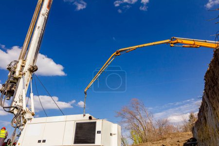 Photo for Truck with pump machine is standing on the edge, cliff of ground, directing exit tube on right direction to bridge foundation, construction site. - Royalty Free Image