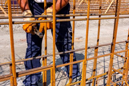 Photo for Worker is tying rebar with wire using pliers, to make a reinforcing frame for concrete beam. Works on construction site - Royalty Free Image