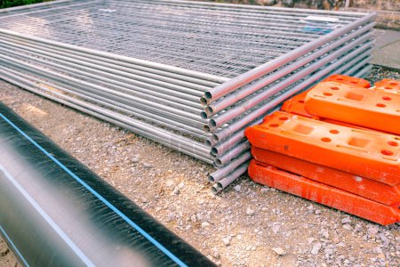 Photo for Pile, heap of galvanized parts for temporary metal fence panels are piled and hollow plastic fence foot on the street, ready for mounting around building site. - Royalty Free Image