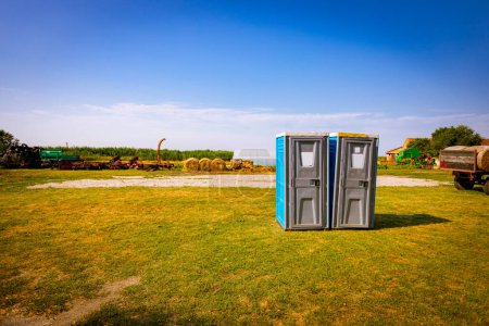 Téléchargez les photos : Deux toilettes mobiles en plastique, toilettes publiques transportables sont placées sur des terres agricoles. - en image libre de droit