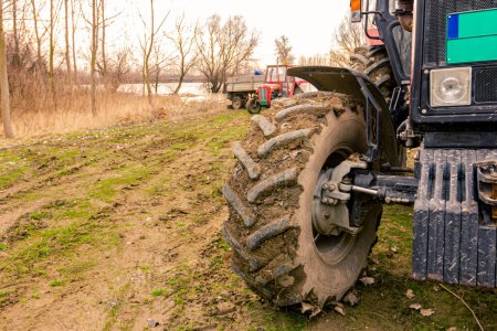 Close-up view of tractor's tire as going on muddy landscape near river coast with water floods.