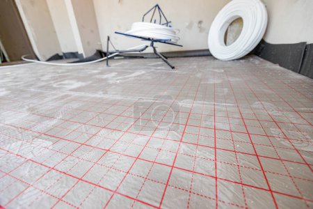 Blick auf geteilte Fläche, mit roten Hilfslinien, Raster, für Hilfe bei der Verlegung der Fußbodenheizung in einem im Bau befindlichen Wohnhaus.