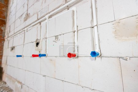 Foto de Nueva instalación de fontanería sin terminar expuestos tubos de PVC blanco montados en la pared. Tubos rojos y azules son para agua caliente y fría. - Imagen libre de derechos