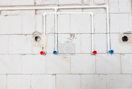Foto de Nueva instalación de fontanería sin terminar expuestos tubos de PVC blanco montados en la pared. Tubos rojos y azules son para agua caliente y fría. - Imagen libre de derechos
