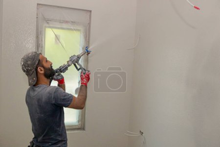Trabajador de la construcción aplica una capa blanca, masilla en la pared, utilizando boquilla, yeso y paredes de revestimiento descremado pulverización mezcla bajo presión.