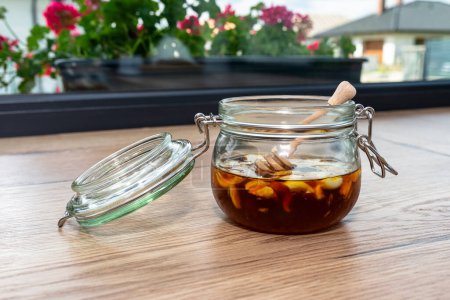 Téléchargez les photos : Ail au miel dans un bocal en verre sur le comptoir de la cuisine avec un bâton de miel en bois. - en image libre de droit