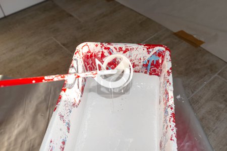 Téléchargez les photos : An open plastic bucket with white paint and a stirrer standing on the floor. - en image libre de droit