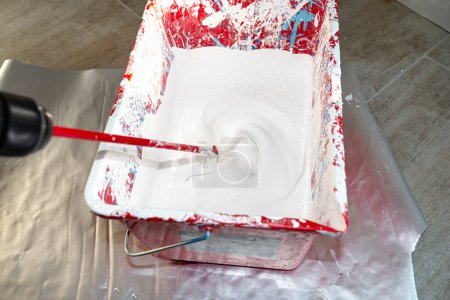 Téléchargez les photos : An open plastic bucket with white paint and a stirrer standing on the floor. - en image libre de droit