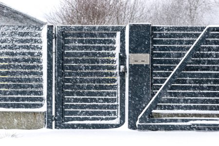 Téléchargez les photos : A modern gate with a letterbox and a wireless card reader, mounted in an anthracite panel fence, covered with snow. - en image libre de droit
