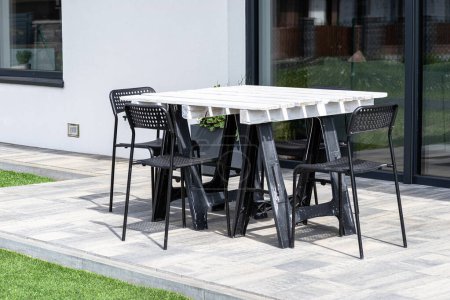 Terrassentisch aus weißer Palette auf Kunststoffböcken stehend, schwarze Kunststoffstühle.