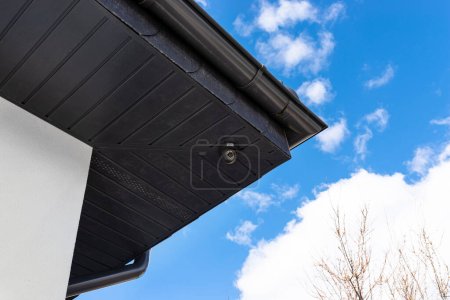 Caméra ronde sans fil montée sur le coin du toit dans le soffit, surveillance d'une maison unifamiliale.