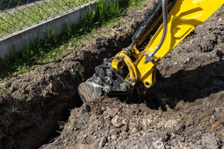 Mini excavadora cavando un agujero en el jardín a lo largo de la cerca de las tuberías de drenaje.