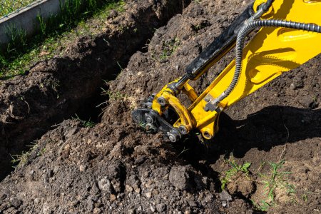 Foto de Mini excavadora cavando un agujero en el jardín a lo largo de la cerca de las tuberías de drenaje. - Imagen libre de derechos