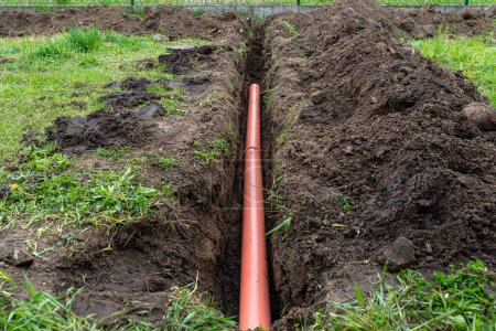 Orangefarbenes PVC-Rohr im Boden vergraben, das mit der Dachrinne verbunden ist und zum Anschluss an das Abwasserrohr verwendet wird.