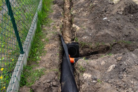 Drainage pipe wrapped in geotextile, inserted into a ditch dug around the house, visible PVC tee.