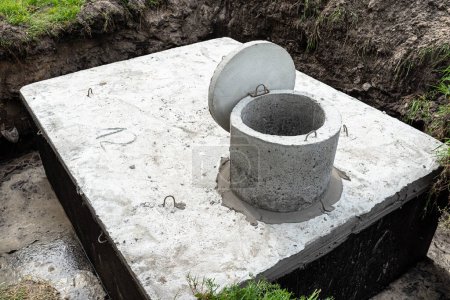 Depósito séptico de hormigón con una capacidad de 10 metros cúbicos colocado en el jardín por la casa, agua visible por debajo.