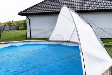 A large expansion pool with a diameter of 3.96 m, set in the yard next to the house, covered with a solar mat.