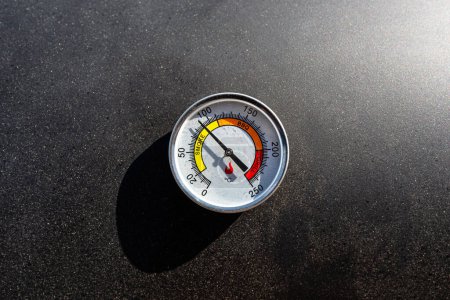 Foto de Un termómetro redondo que muestra 90 grados Celsius colocado en una parrilla de carbón. - Imagen libre de derechos