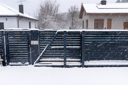 Photo for A modern gate with a letterbox and a wireless card reader, mounted in an anthracite panel fence, covered with snow. - Royalty Free Image