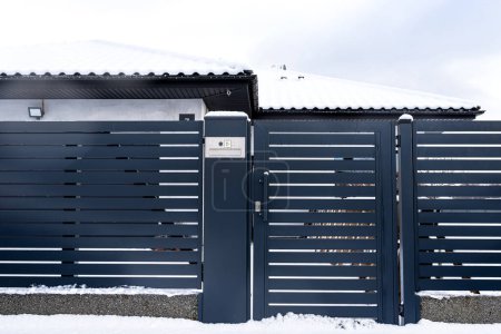 Téléchargez les photos : Un portail moderne avec une boîte aux lettres et un lecteur de carte sans fil, monté dans une clôture à panneaux anthracite, recouvert de neige. - en image libre de droit