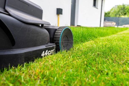 Photo for Mowing grass with an electric, powered mower, with a cutting width of 44 cm, visible mown rows. - Royalty Free Image