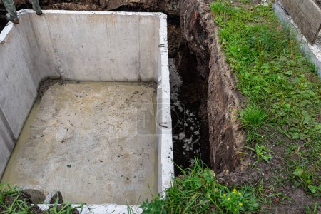 Concrete septic tank with a capacity of 10 m3 located in the garden next to the house, without a cover.