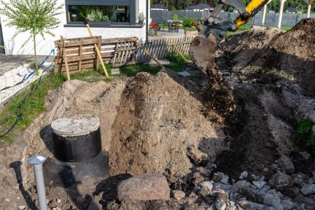 Usando una excavadora para enterrar un tanque séptico de hormigón de 10 m3 ubicado en el jardín junto a la casa.