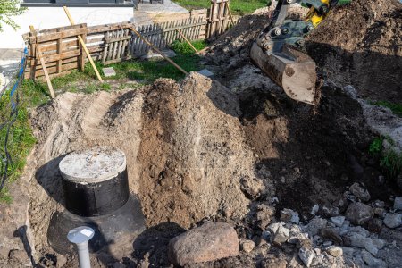 Utilisation d'une excavatrice pour enterrer une fosse septique en béton de 10 m3 située dans le jardin à côté de la maison.
